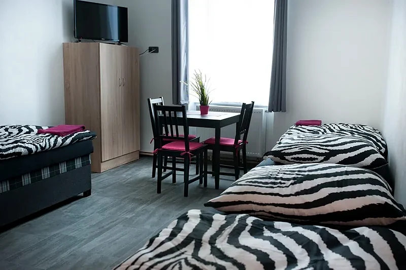 Světlý pokoj s lůžky, jídelním stolem, skříní a televizorem